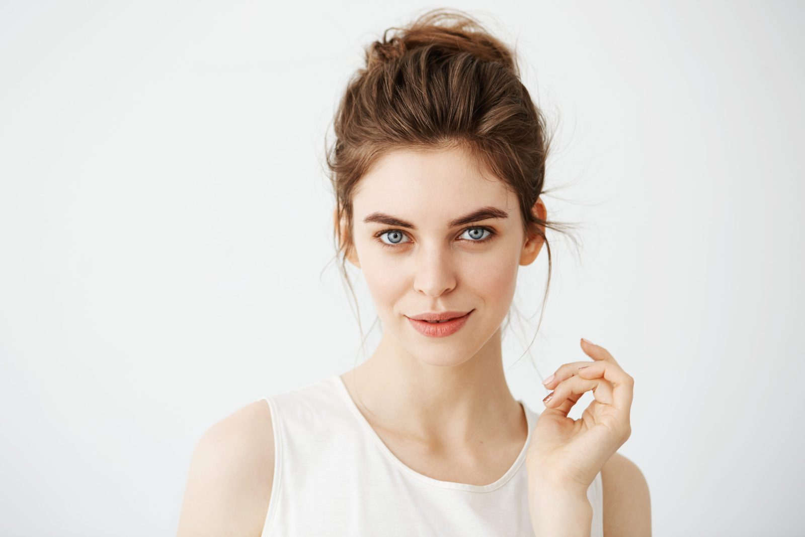 Portrait of young beautiful playful girl with bun looking at camera posing over white background. Copy space.